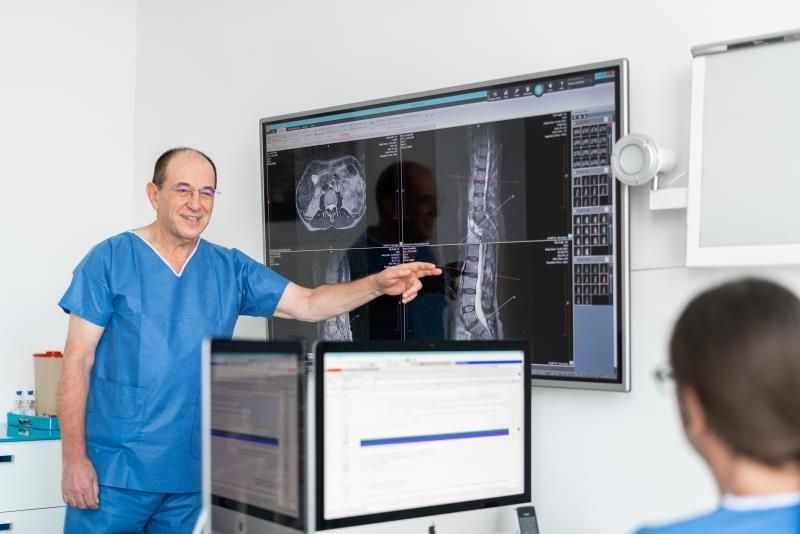 Ein Mann im blauen OP-Kittel zeigt auf einen Computerbildschirm.