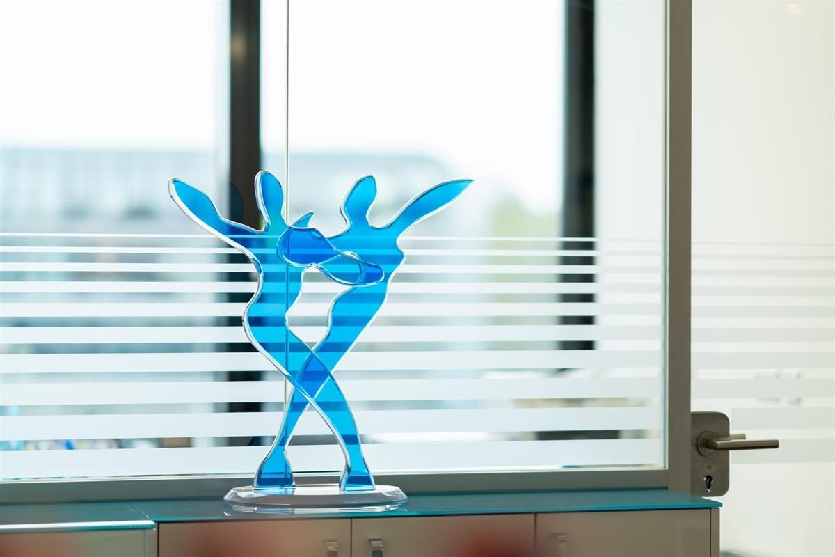 Eine blaue Statue von zwei tanzenden Menschen sitzt auf einem Tisch vor einem Fenster.