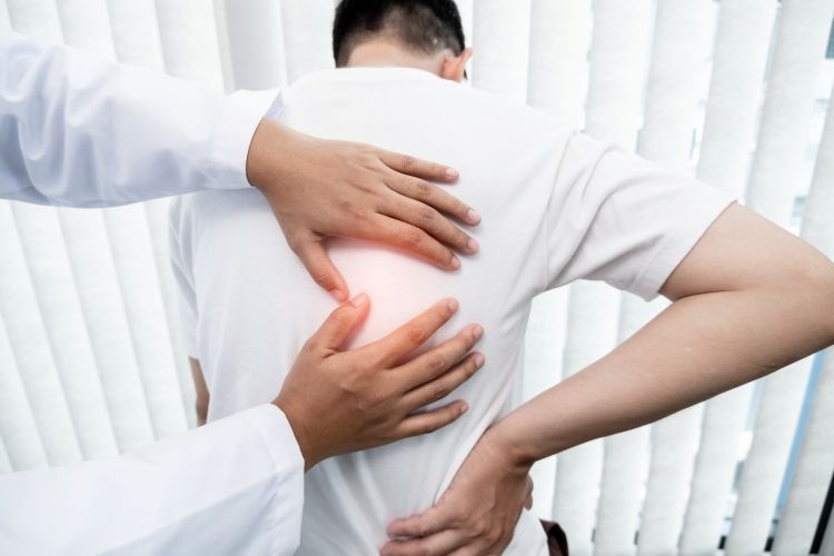 Ein Arzt tastet den schmerzenden Rücken eines Patienten ab. Symbolbild für die Leistungen unserer orthopädischen Privatpraxis in Köln.