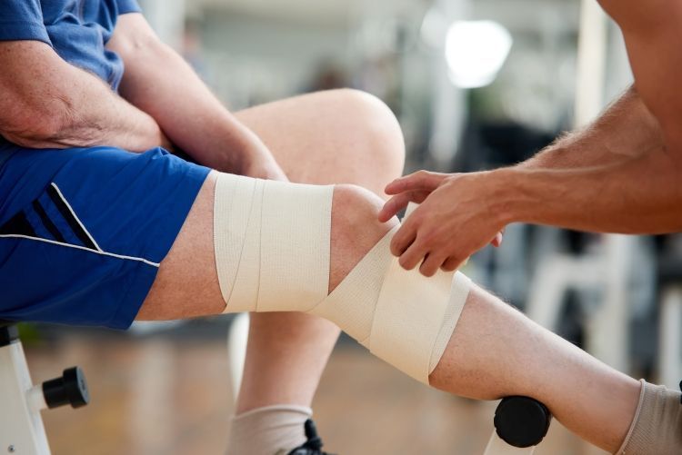 Einem Knie wird eine Bandage angelegt. Unsere Orthopädie Privatpraxis ist auf die Behandlung von Sportverletzungen spezialisiert.