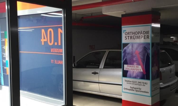In einem Parkhaus steht ein Auto neben einem Schild mit der Aufschrift „Orthopädie Strumper“.