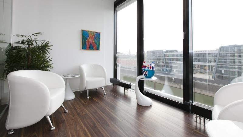 Ein Wartezimmer mit zwei weißen Stühlen und einem Tisch vor einem großen Fenster.