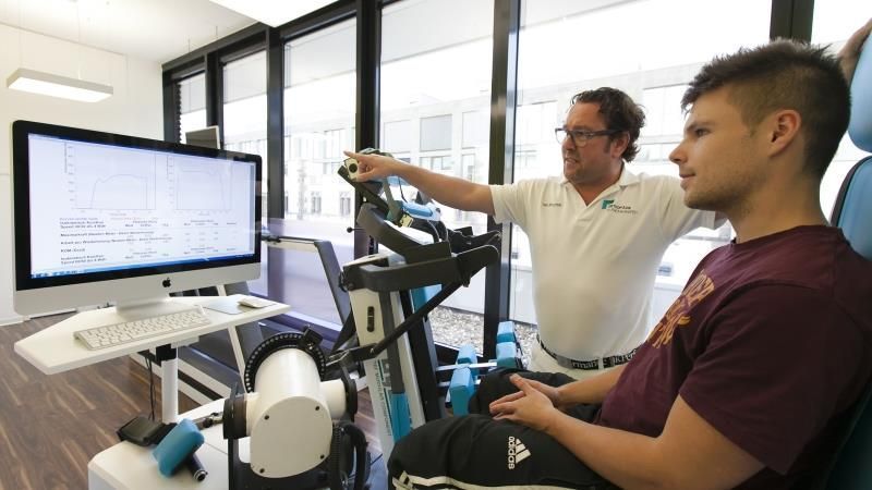 Ein Mann sitzt vor einem Computer, während ein anderer Mann hinter ihm steht.