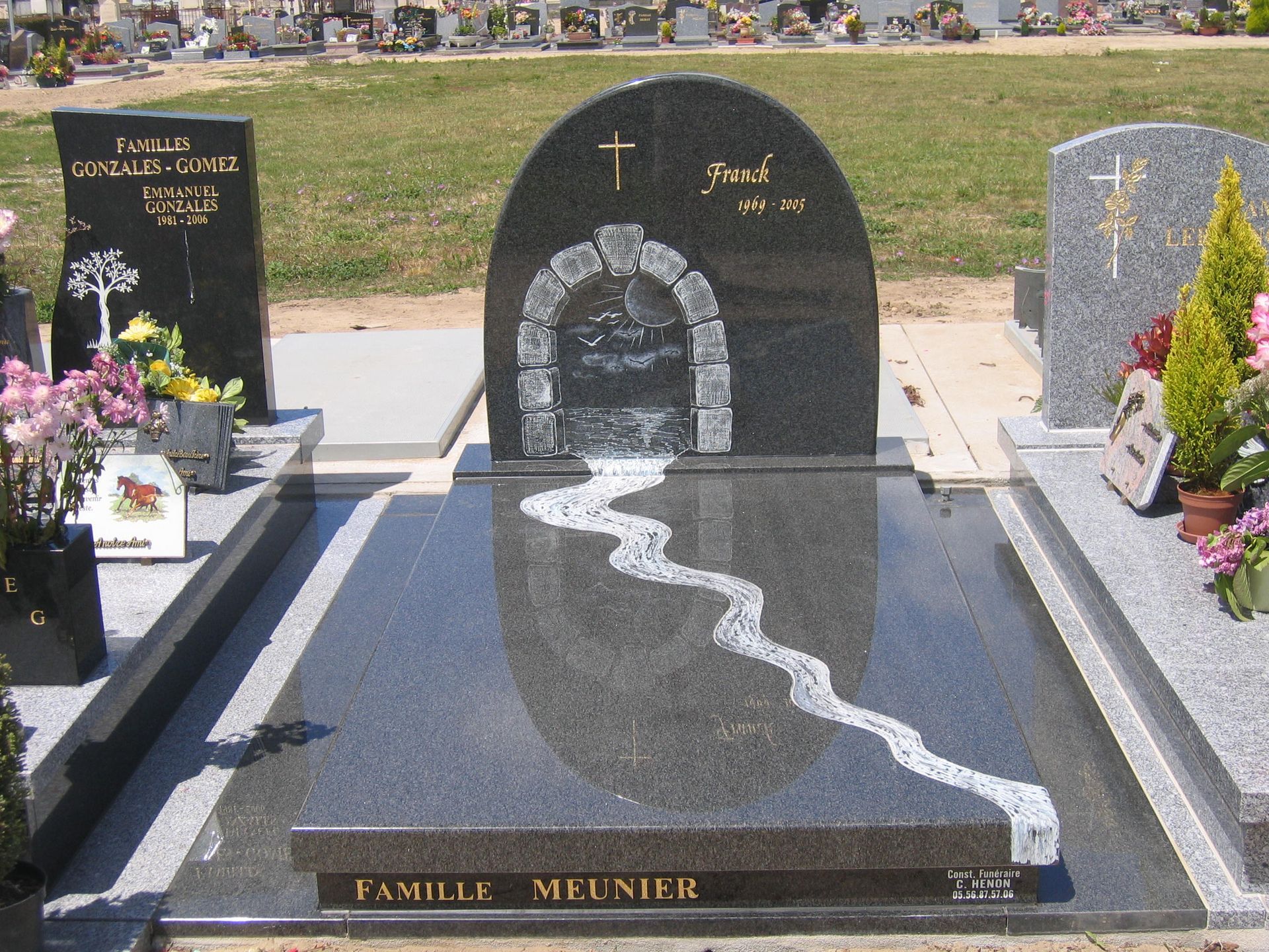Pierre tombale en granit noir avec arche, croix et motif de rivière blanche sinueuse ; pierre tombale familiale dans un cimetière.