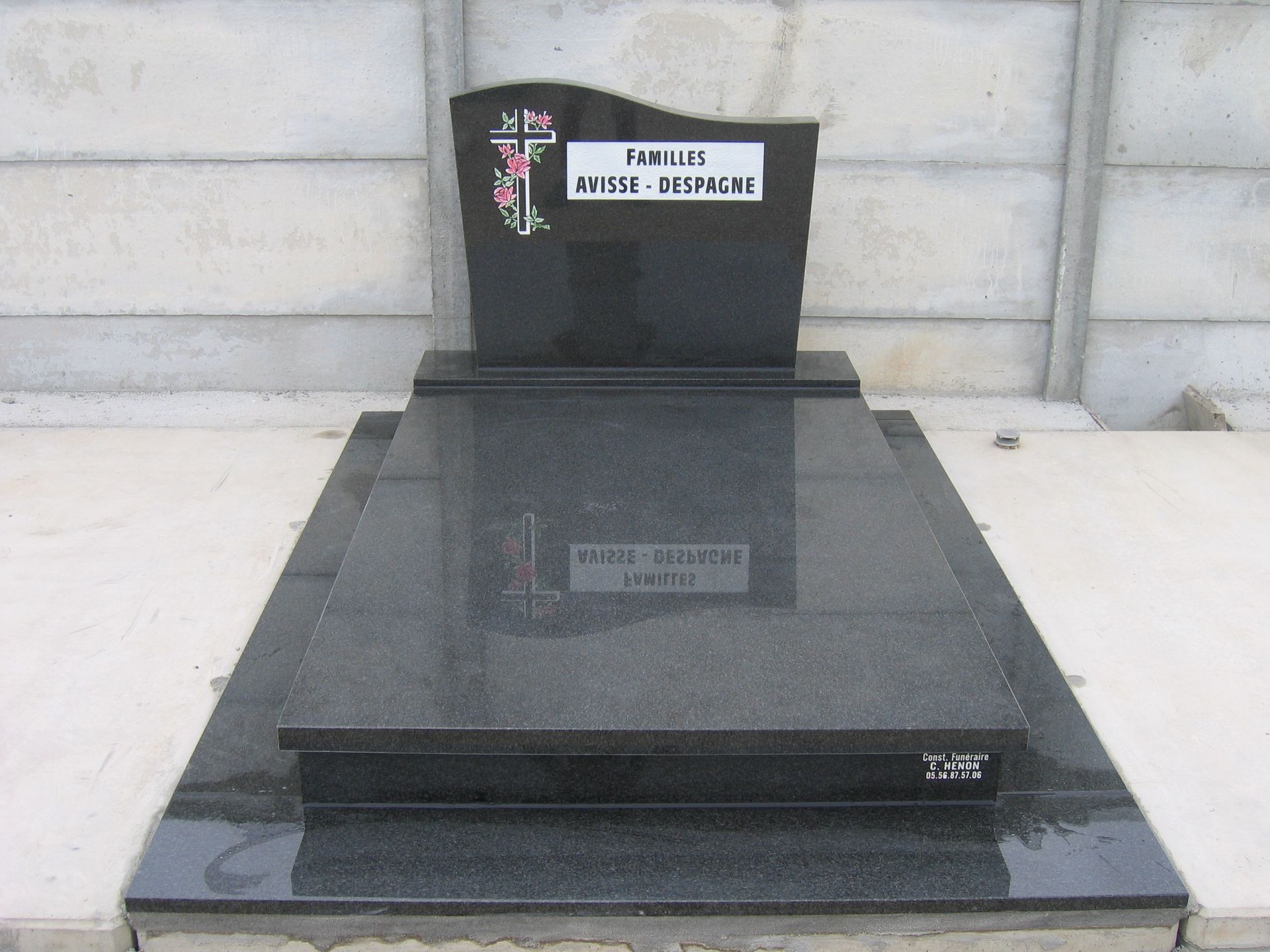 Pierre tombale en granit noir avec croix et inscriptions.