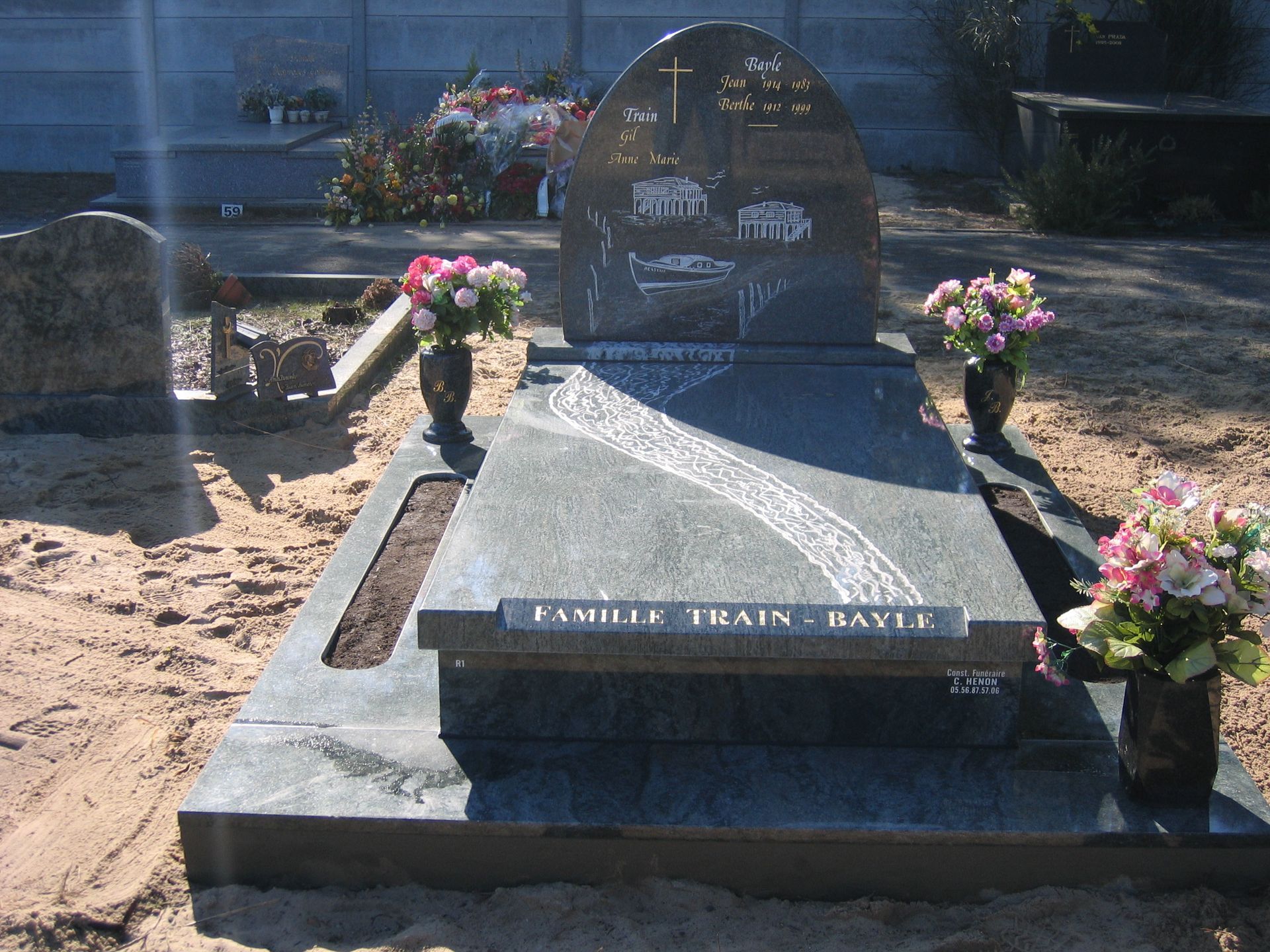 Pierre tombale en granit ornée de fleurs, probablement dans un cimetière. Elle comporte une croix et une inscription nominative.