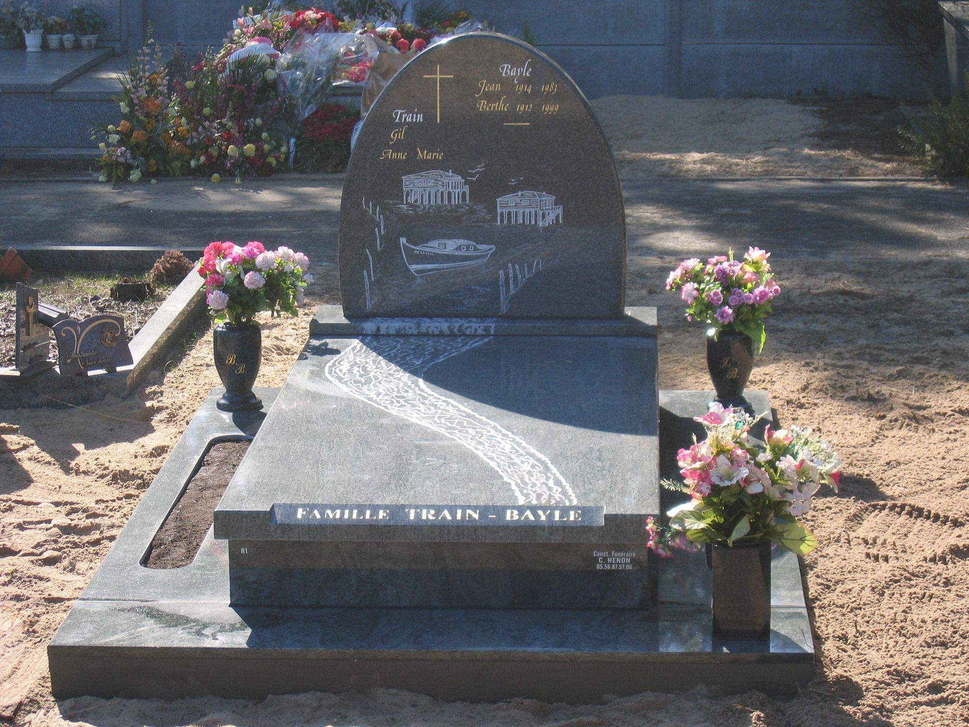 Tombe avec pierre tombale noire, scène gravée, fleurs et texte « Famille Twain-Davis » dans le cimetière.