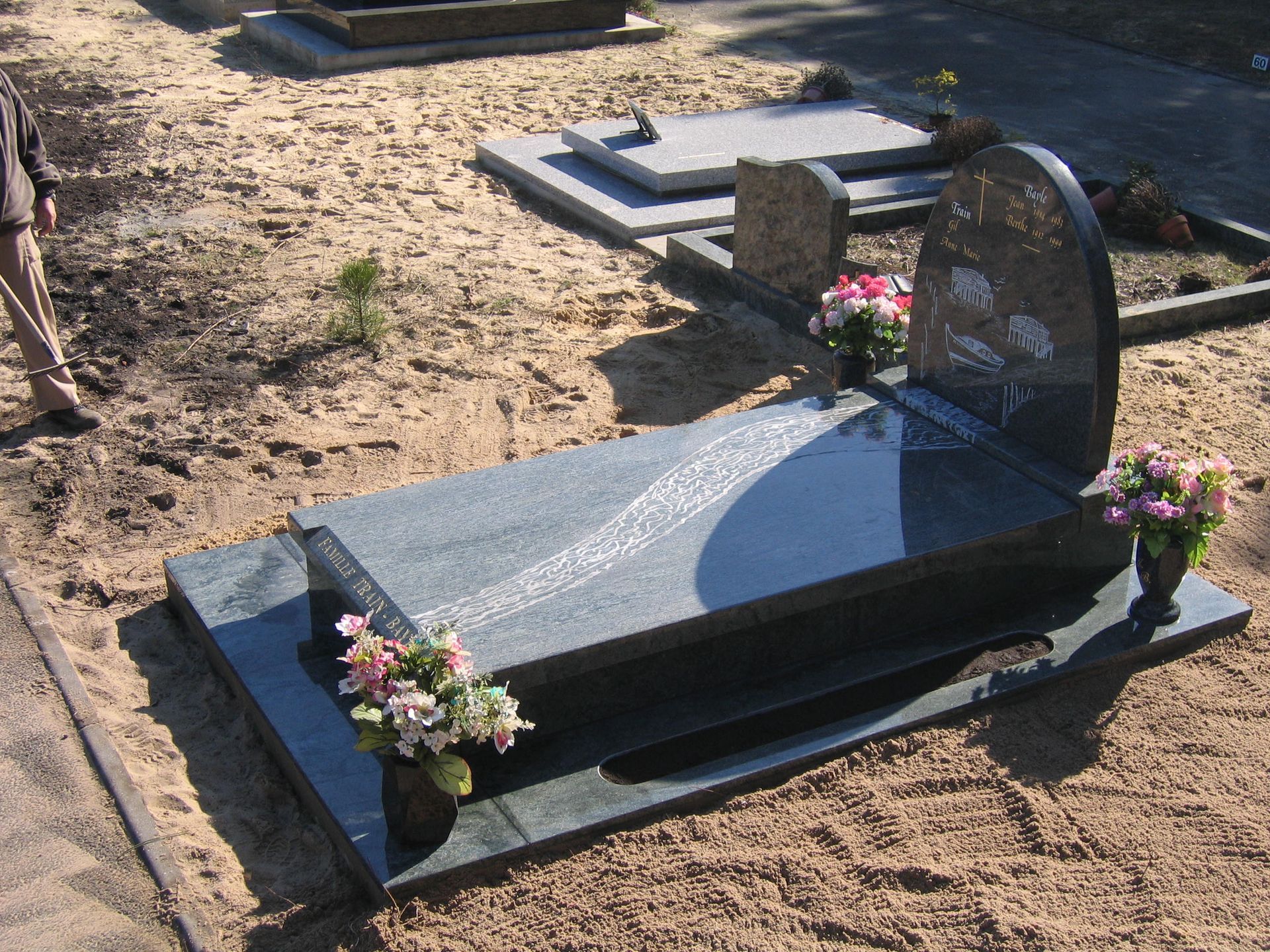 Pierre tombale avec fleurs ; pierre de granit noir dans un cimetière sablonneux.