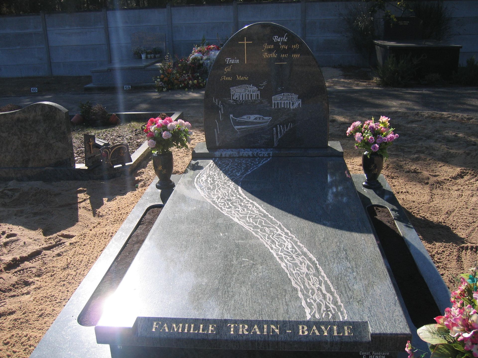 Pierre tombale dans un cimetière avec compositions florales, détails gravés et inscription « Famille Train - Bayle ».