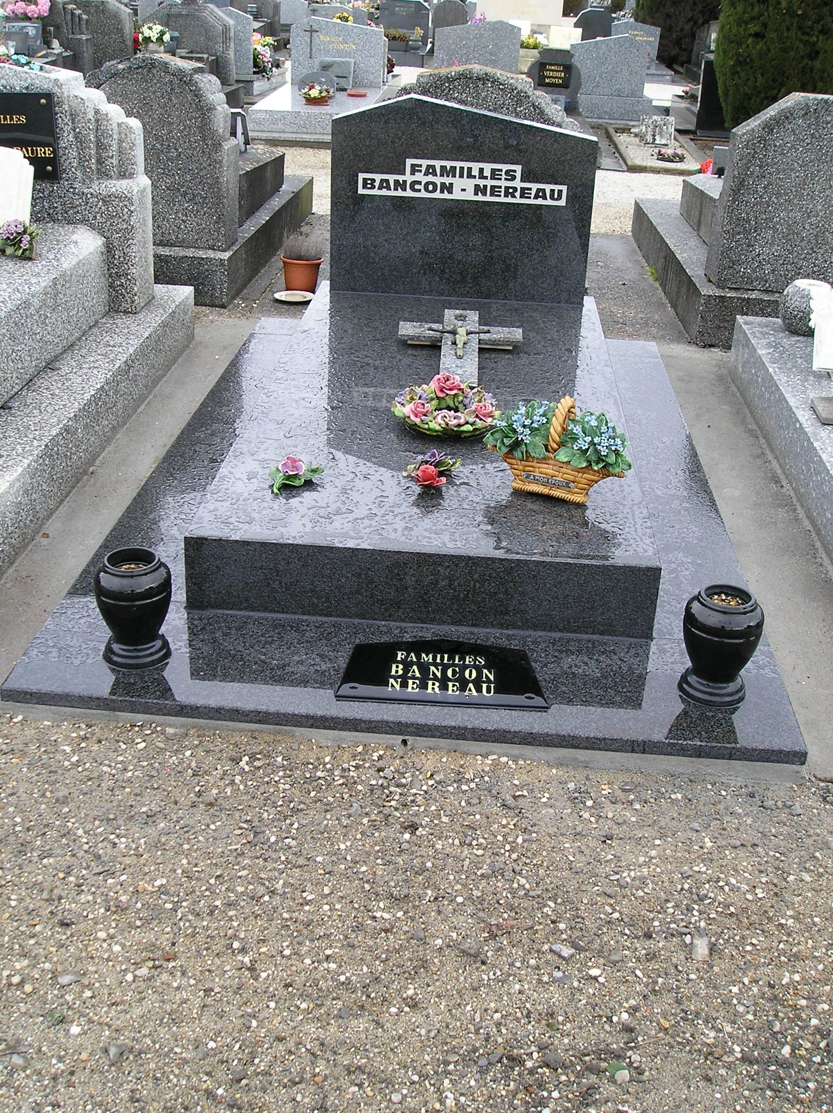 Pierre tombale dans un cimetière, avec fleurs et vases. Elle est en granit foncé.