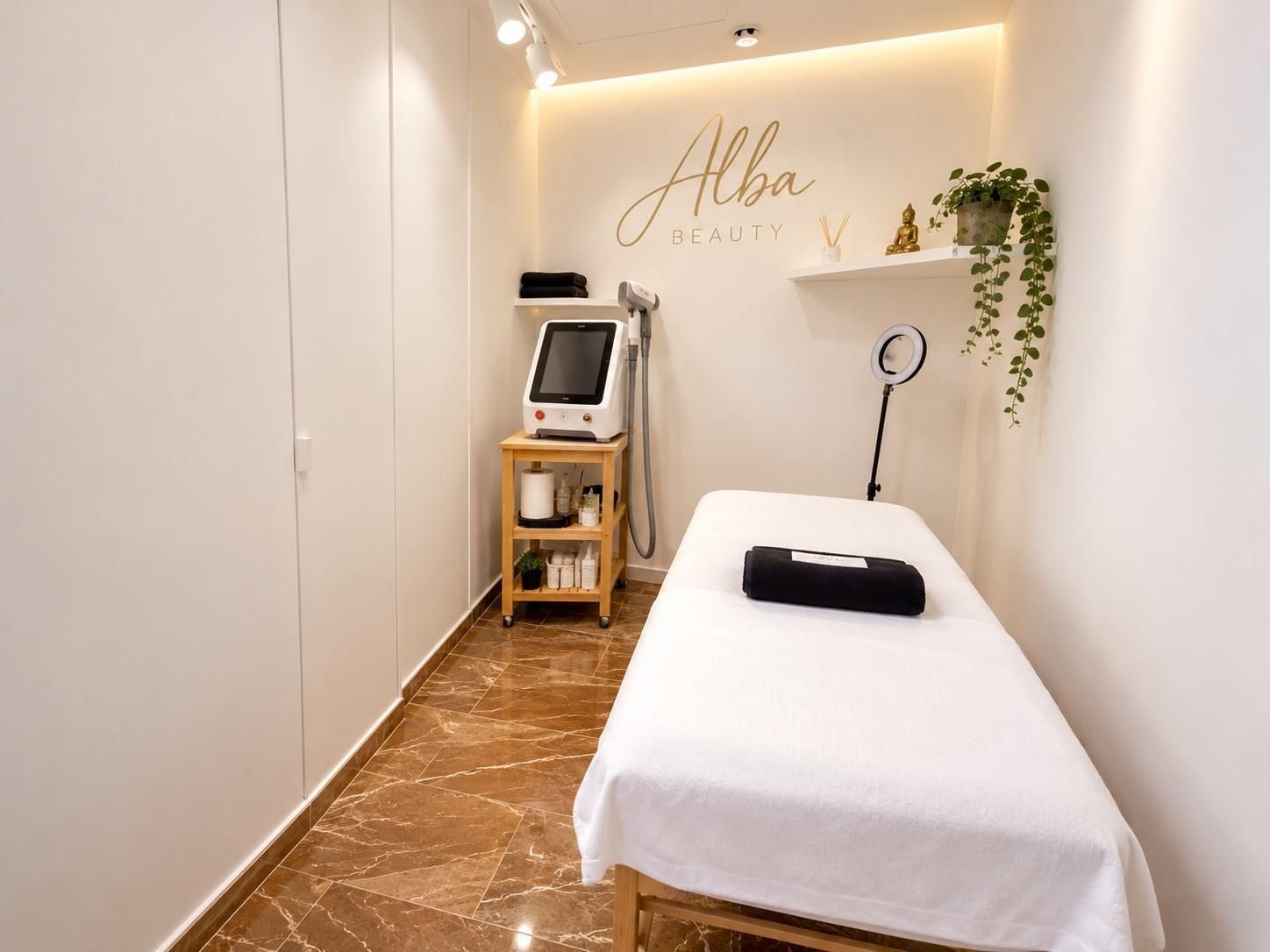 Sala de tratamientos de spa minimalista con camilla blanca, iluminación cálida, aparato facial y planta colgante