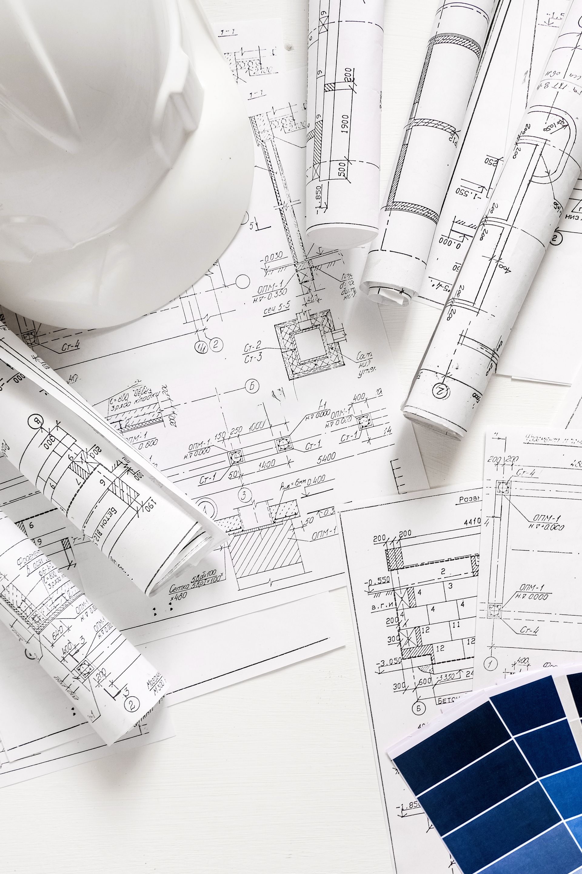Casque de chantier, plans roulés et échantillons de couleurs sur une surface blanche, suggérant une planification architecturale ou de construction.