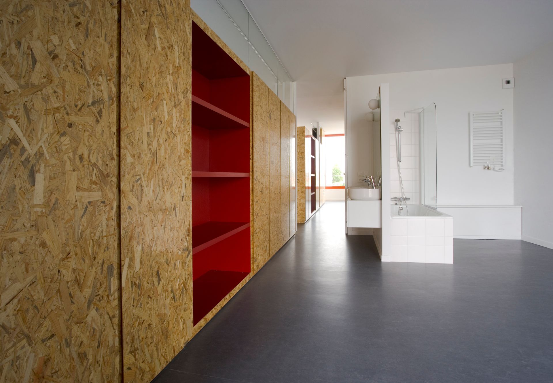 Intérieur avec boiseries, étagères rouges, salle de bains blanche et sol gris.