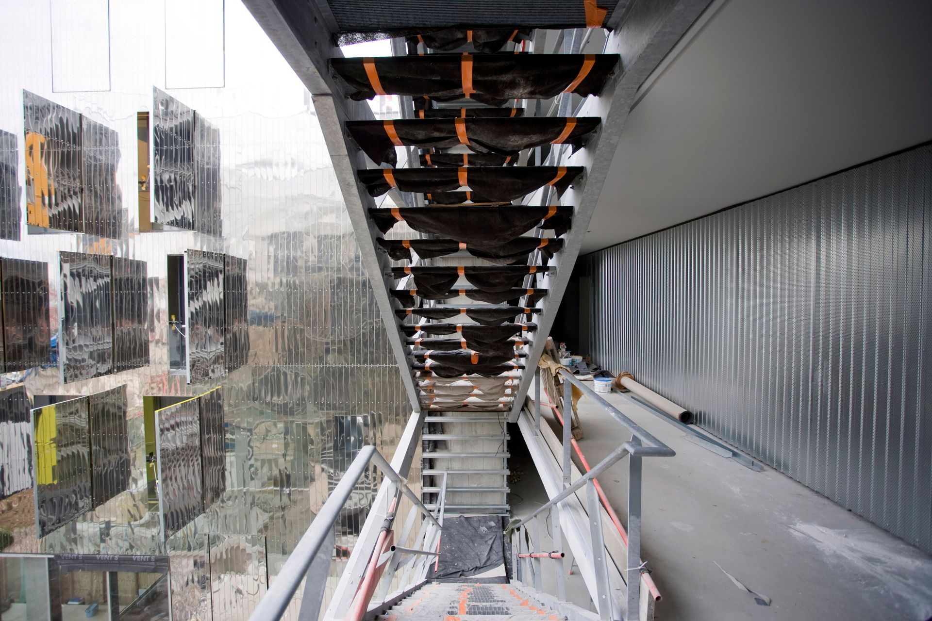 Escalier avec panneaux réfléchissants et parois métalliques. La lumière du soleil se reflète sur les surfaces.