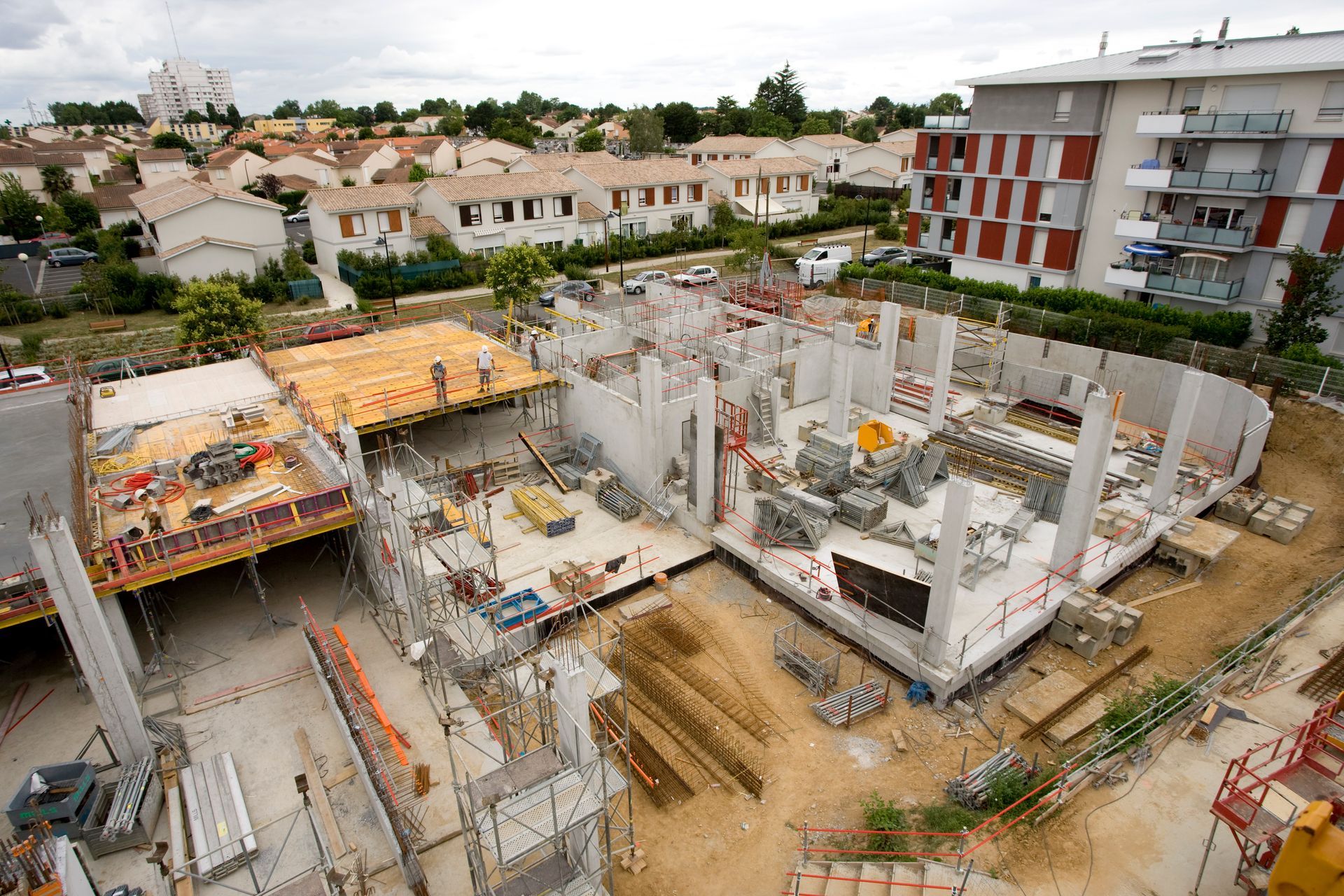 Chantier de construction avec structures en béton et bâtiments résidentiels environnants.