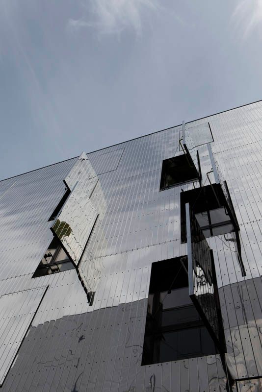 Façade d'un bâtiment avec panneaux réfléchissants et ouverts sous un ciel nuageux.
