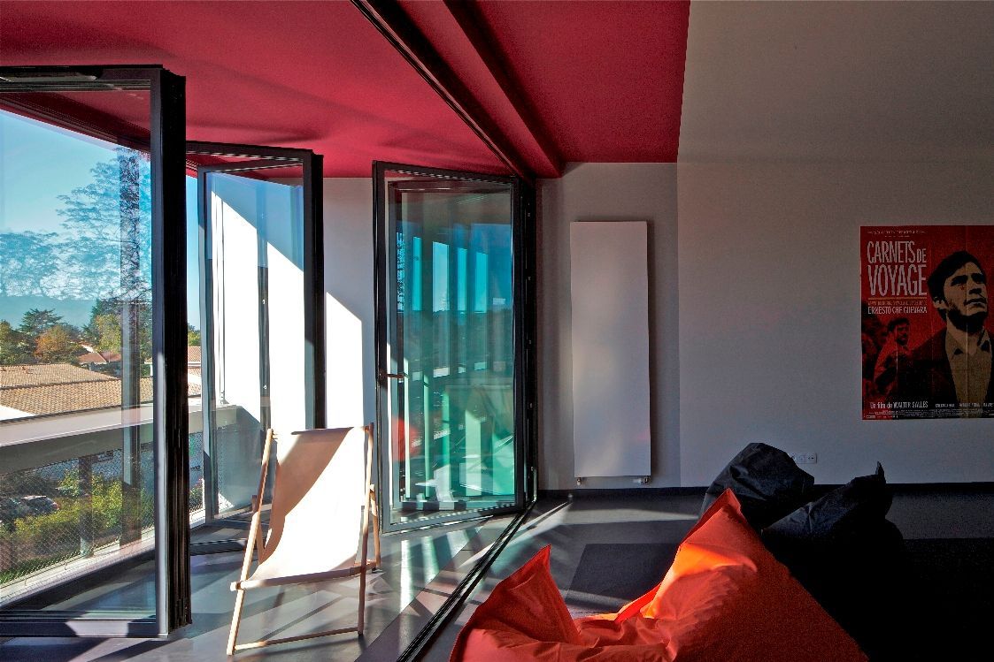 Intérieur de la pièce avec de grandes fenêtres, un plafond rouge, un pouf orange et une affiche au mur.