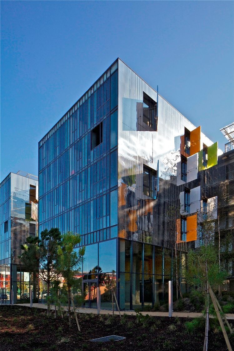 Bâtiment moderne avec façade en miroir et en verre, fond de ciel bleu.