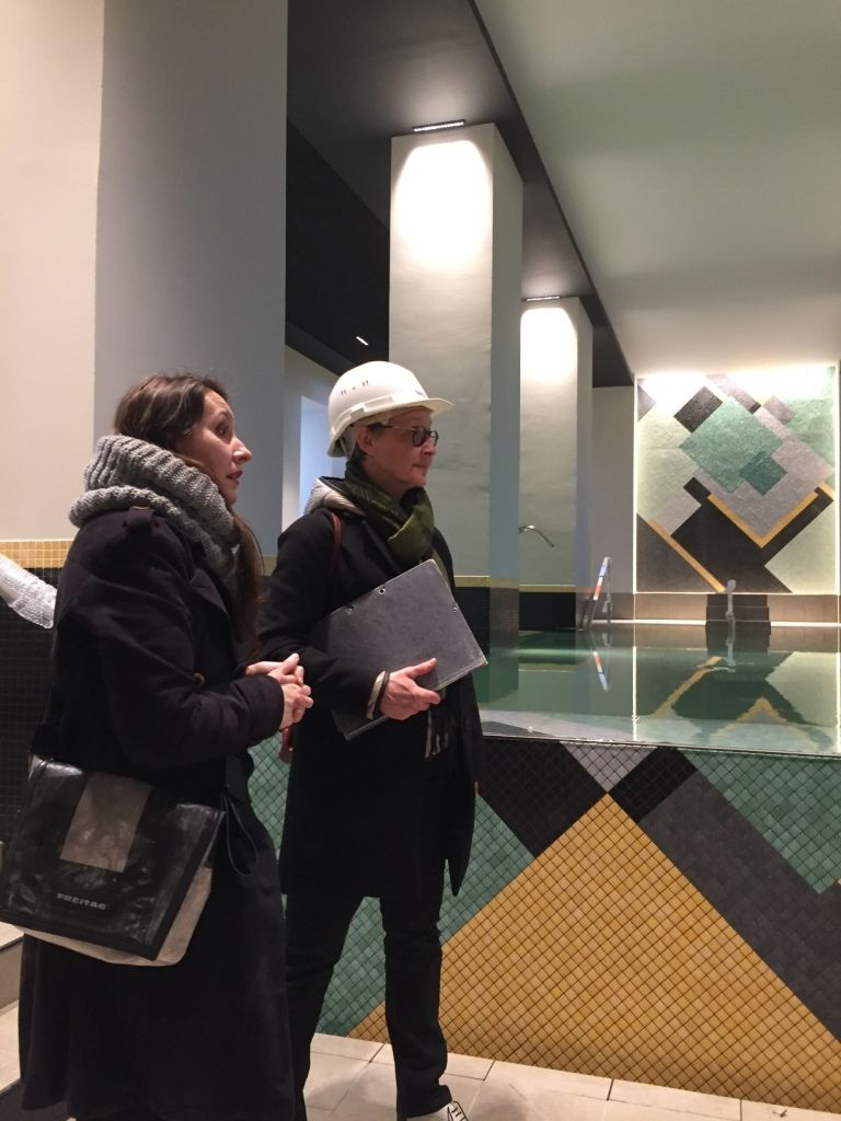 Deux personnes inspectent une zone carrelée autour d'une piscine. L'une porte un casque et tient un dossier.