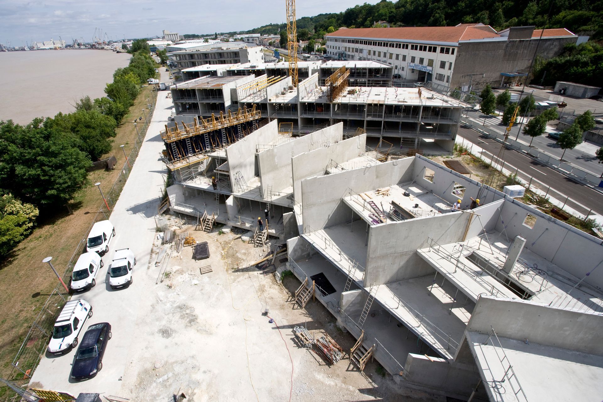 Chantier de construction avec des bâtiments en béton inachevés et une grue près d'une rivière.