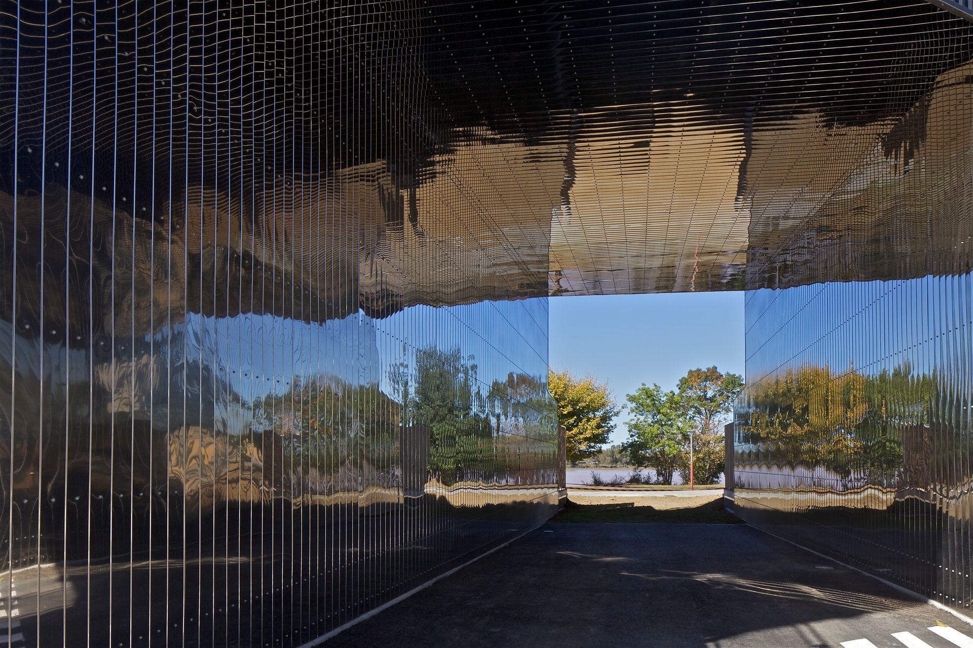 Structure réfléchissante noire avec des arbres et le ciel visibles à travers une ouverture.