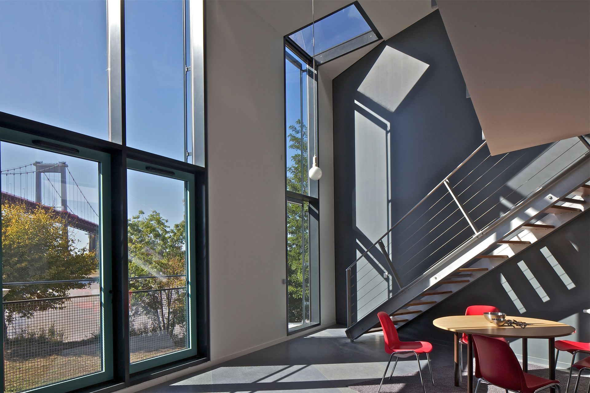 Intérieur moderne avec de grandes fenêtres, des escaliers, des chaises rouges et une vue sur le pont.