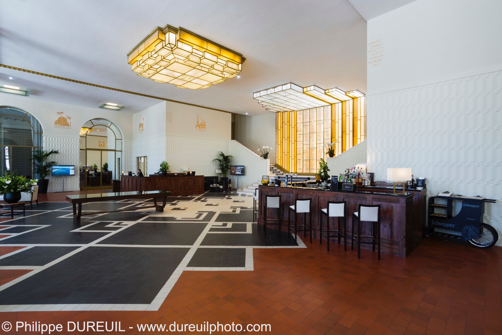 Intérieur du hall avec un bar, un sol au design géométrique et des lustres ornés.