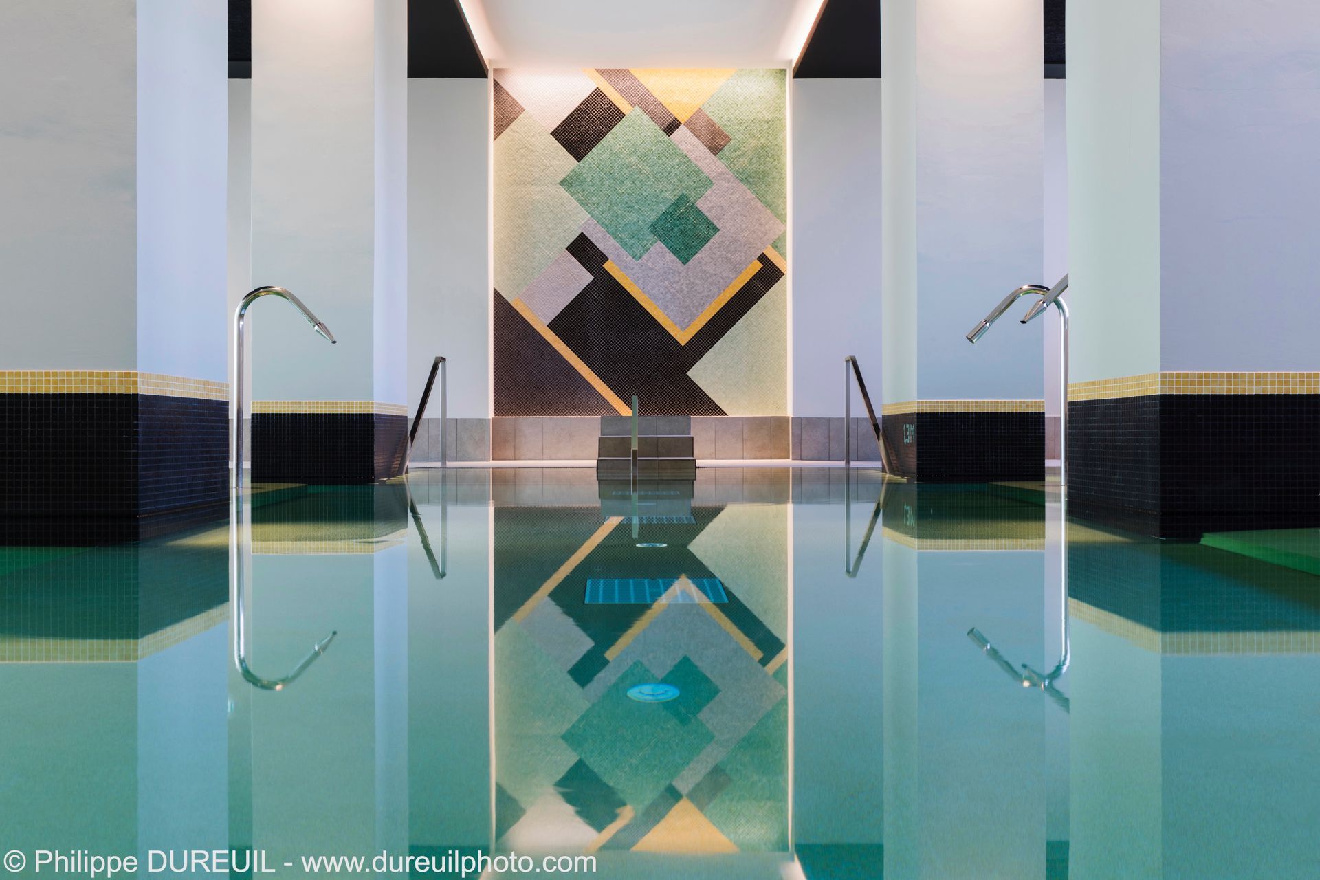 Piscine intérieure avec carrelage géométrique et lumières réfléchissantes au plafond.