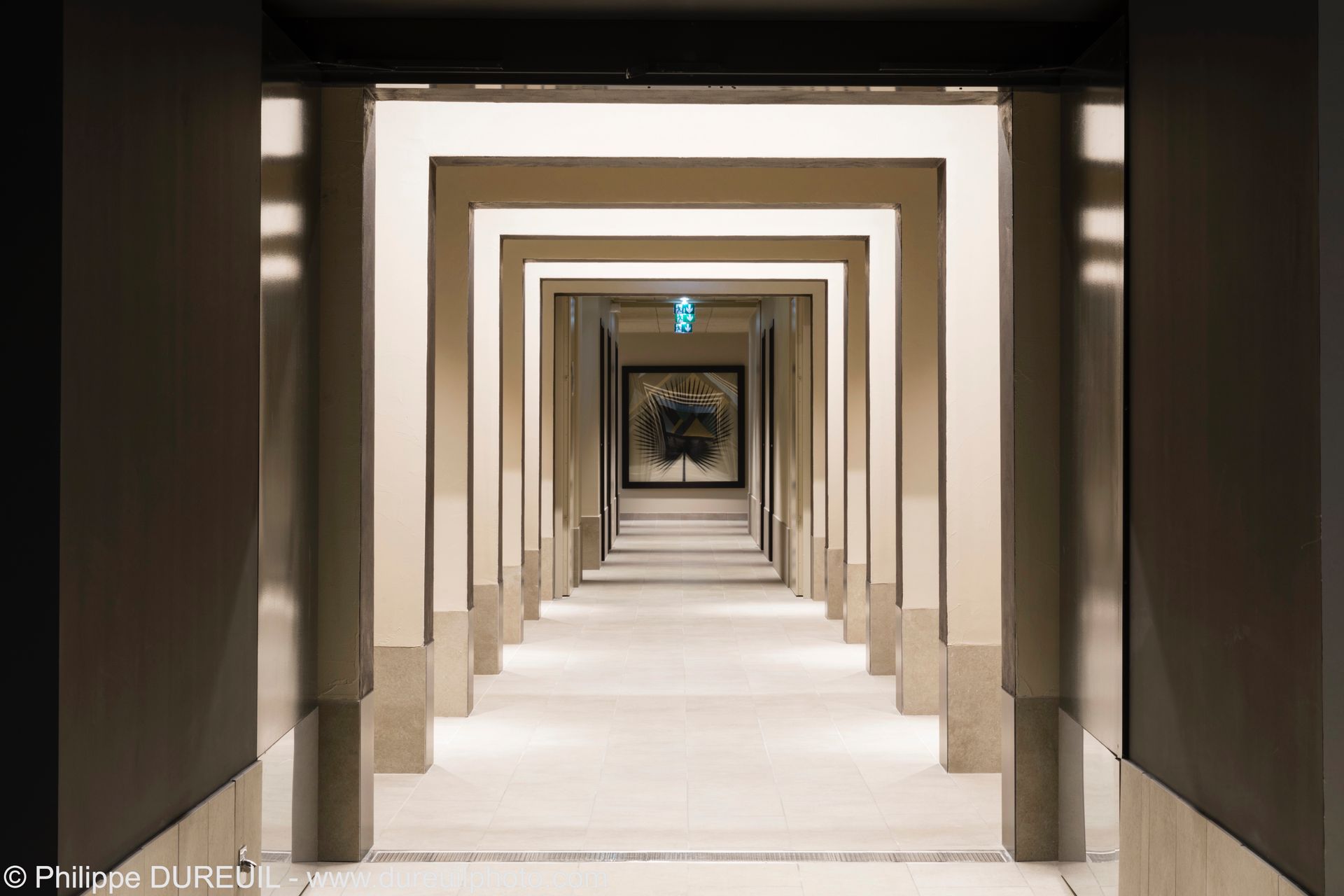 Couloir avec des portes carrées répétées menant à une image encadrée d'un arbre.