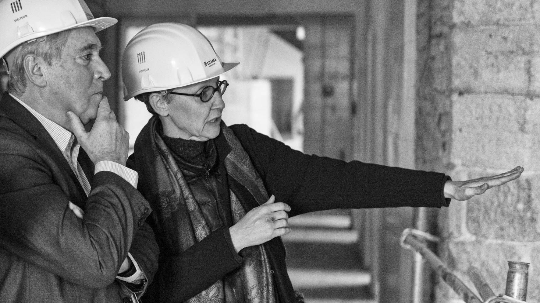 Deux personnes portant des casques de sécurité examinent un mur de pierre sur un chantier de construction.