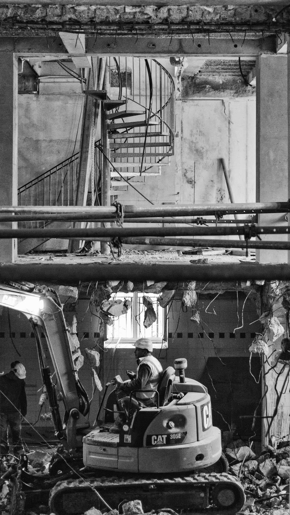 Chantier de démolition : excavatrice dans les décombres, escalier en colimaçon exposé et structure intérieure visible.
