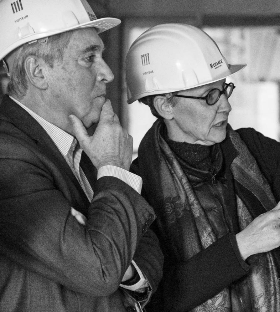 Une femme à lunettes sourit, vêtue d'un foulard et d'une veste. Ses cheveux sont relevés et l'arrière-plan est flou.