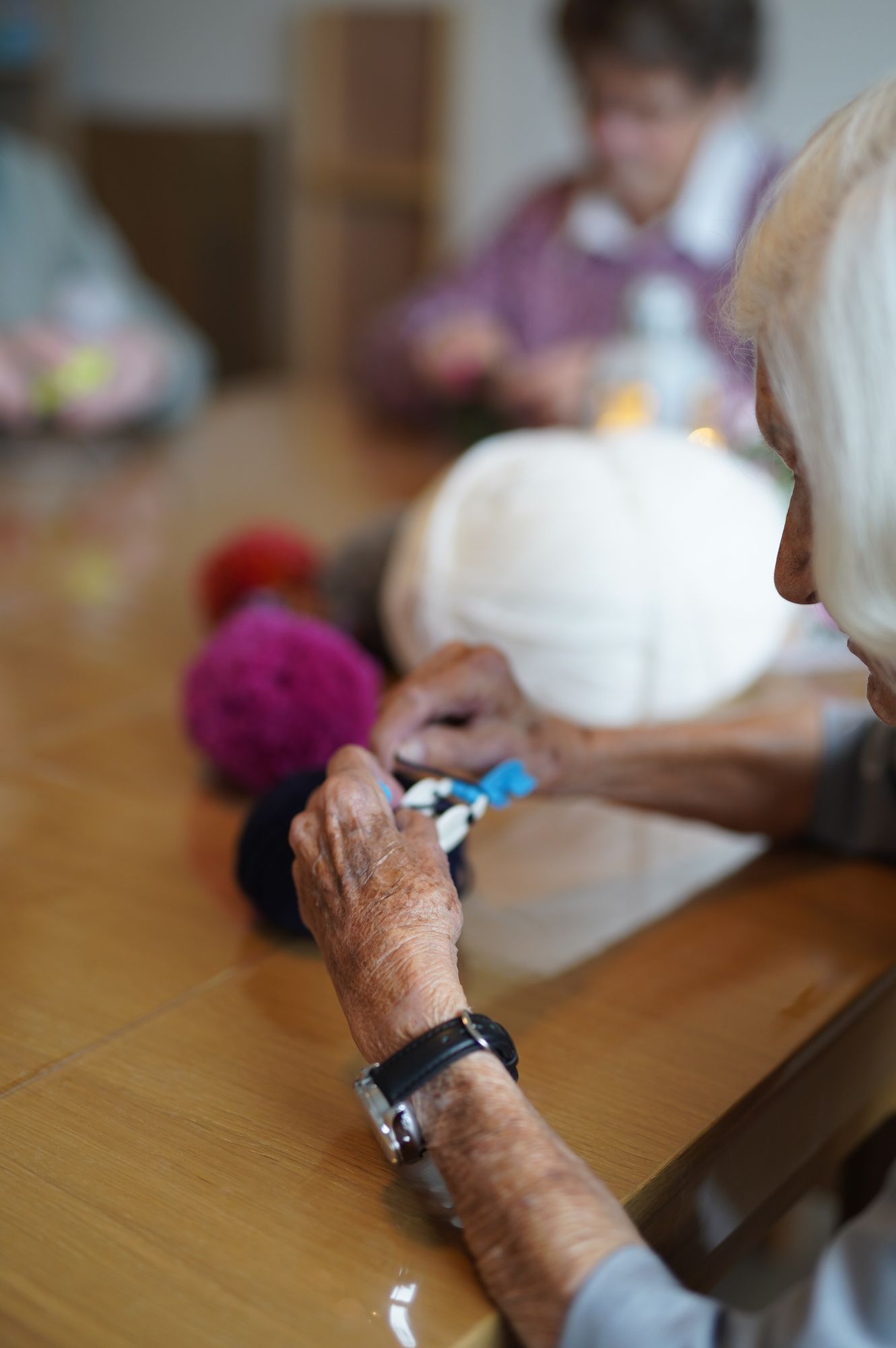 Drei Frauen basteln an einem Tisch. Eine ältere Frau klebt Papier. Andere lächeln, umgeben von Papierstreifen, Getränken und einer Laterne.
