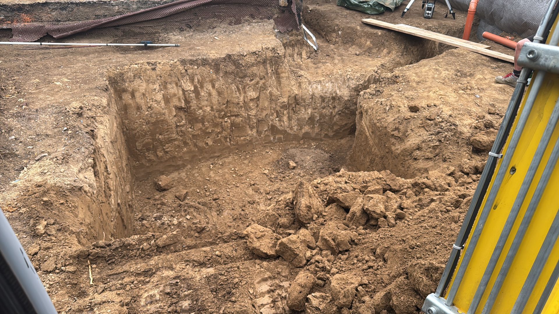 Große Baugrube auf einer Baustelle mit freiliegendem Erdreich und Baumaschinen an den Rändern