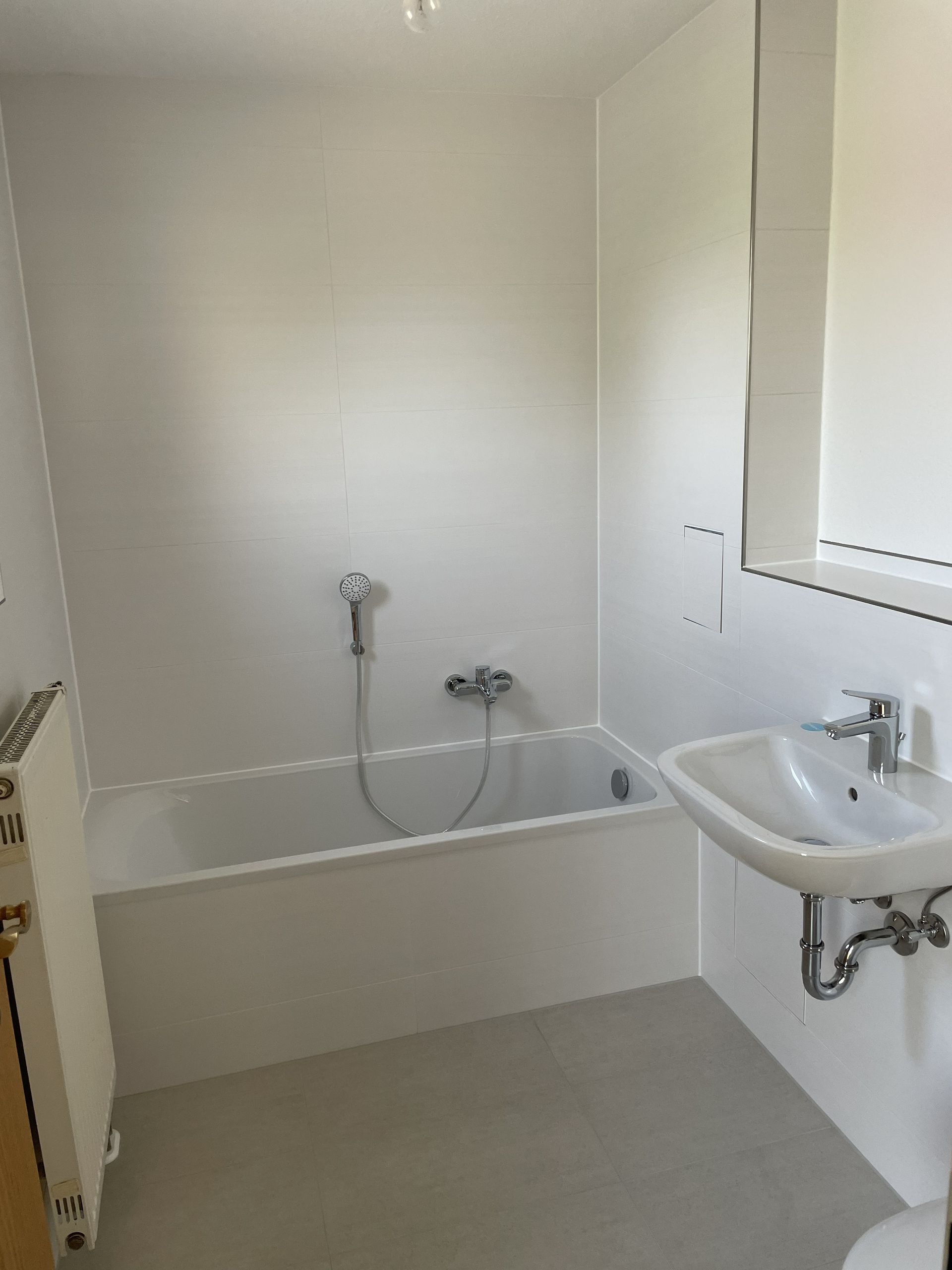 Kleines weißes Badezimmer mit Badewanne, wandmontierter Dusche und Eckwaschbecken.