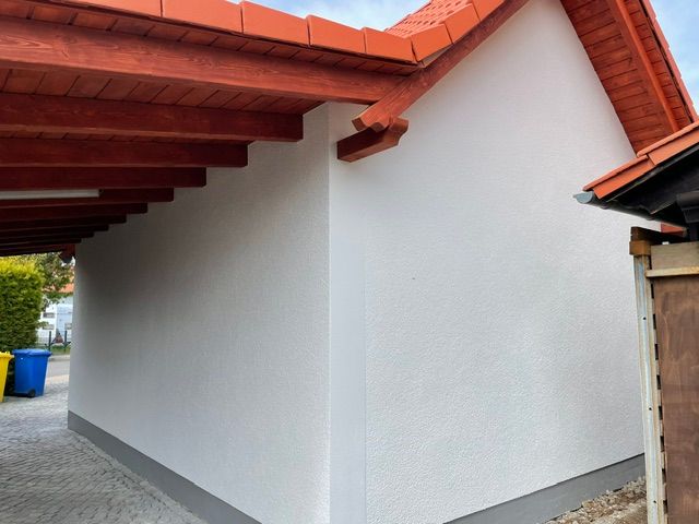 Weiße Außenwand unter einem roten Ziegeldach neben einer gepflasterten Auffahrt