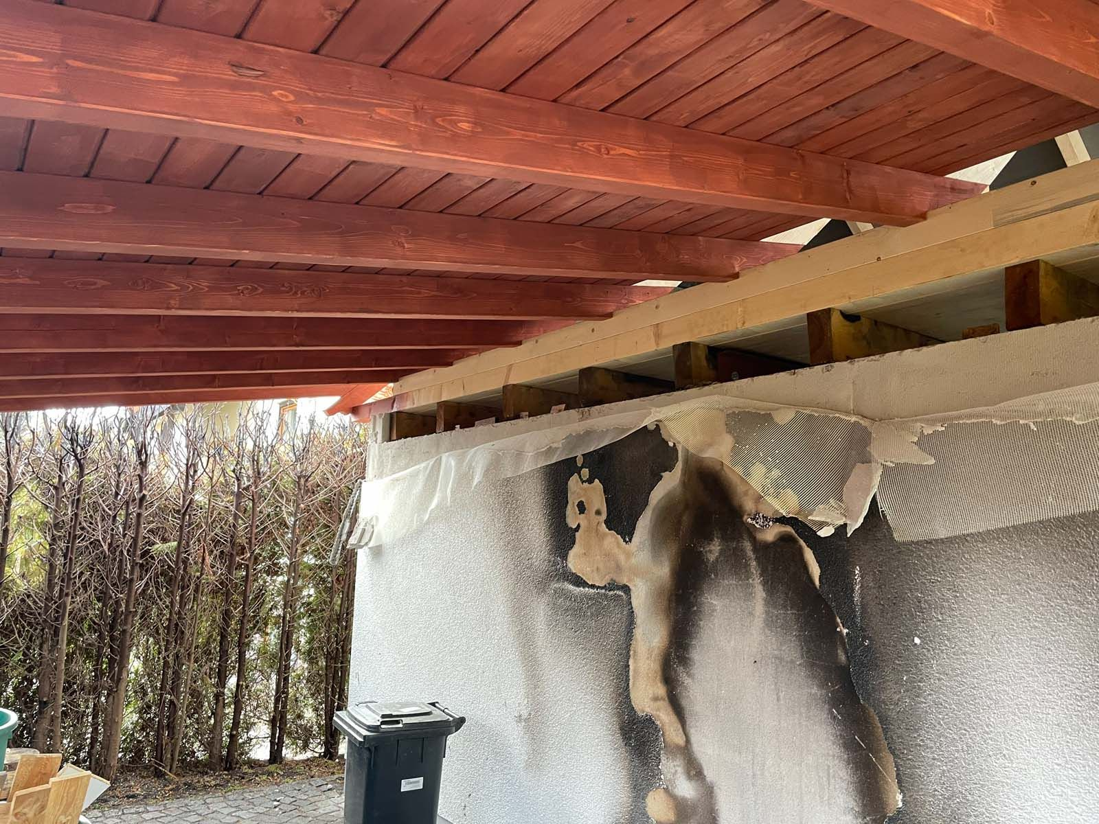 Teilweise abgerissenes Wandgemälde unter einem Holzdach, im Hintergrund Bäume und eine Mülltonne.