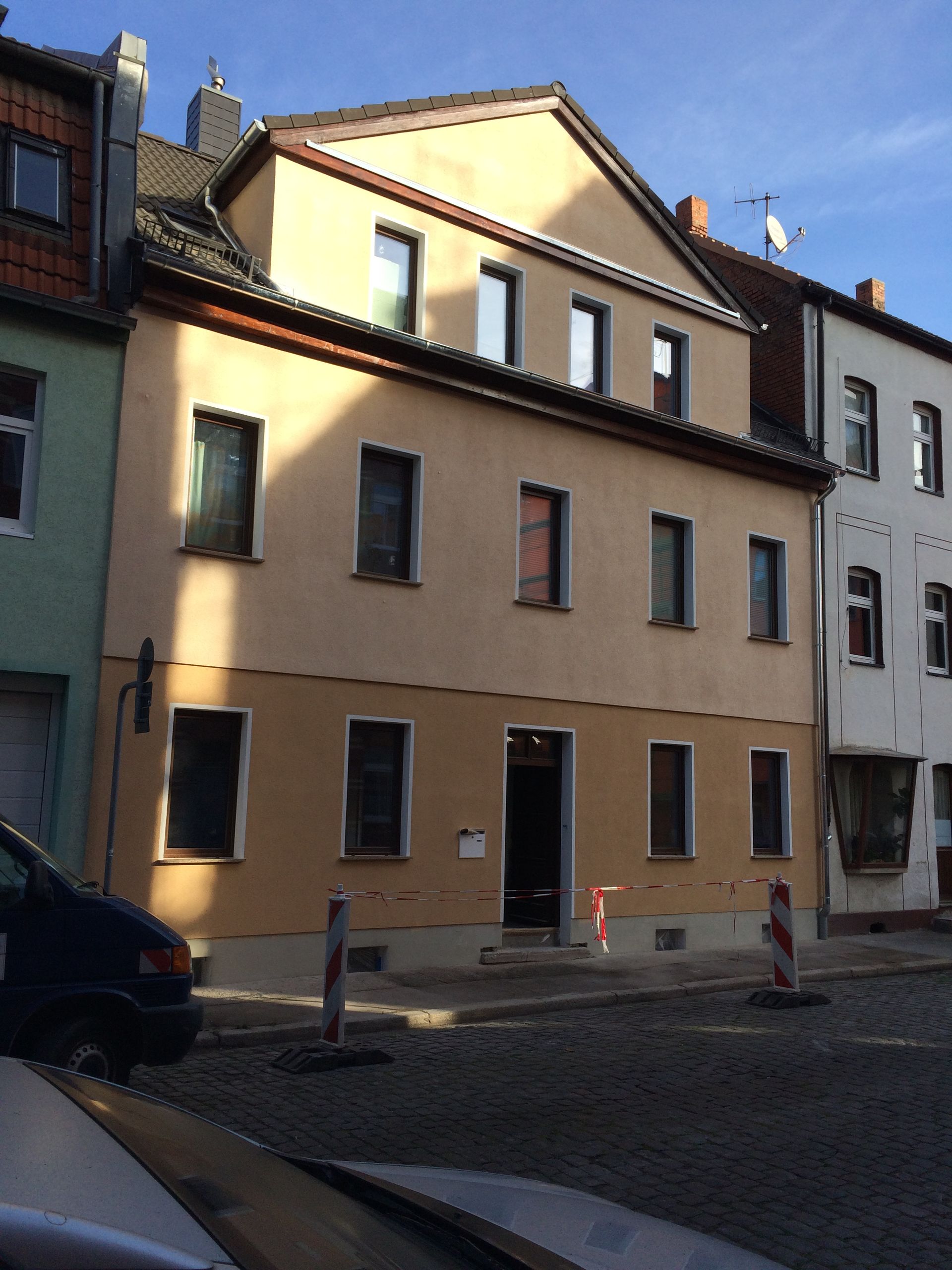 Sonnendurchflutetes beigefarbenes Stadthaus in einer Kopfsteinpflasterstraße mit daneben geparkten Autos