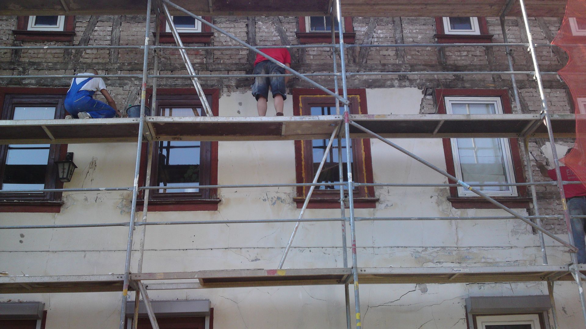 Arbeiter auf einem Gerüst reparieren die Fassade eines Backsteingebäudes