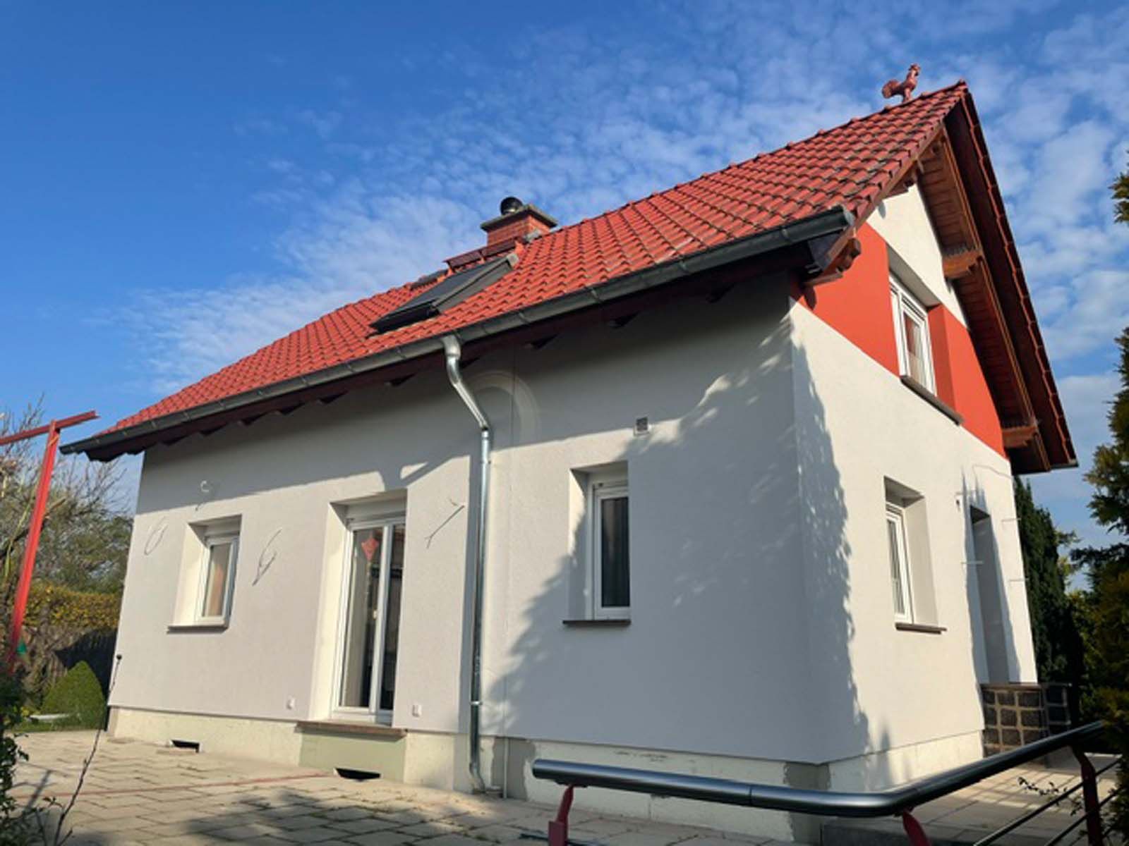 Weißes Haus mit rotem Ziegeldach und kleinen Fenstern unter blauem Himmel