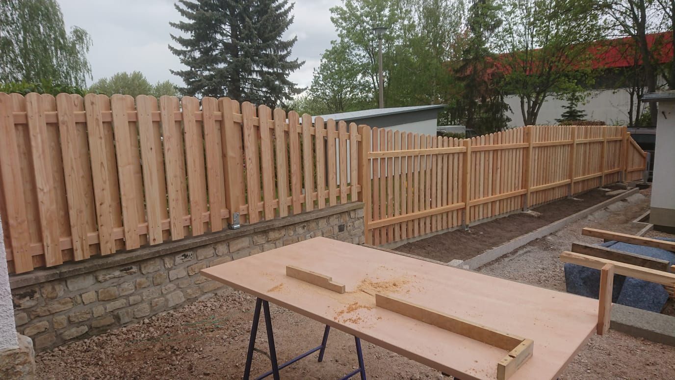Hinterhof mit im Bau befindlichem Holzzaun, Werkzeug und Holz auf einer Werkbank, bewölkter Tag