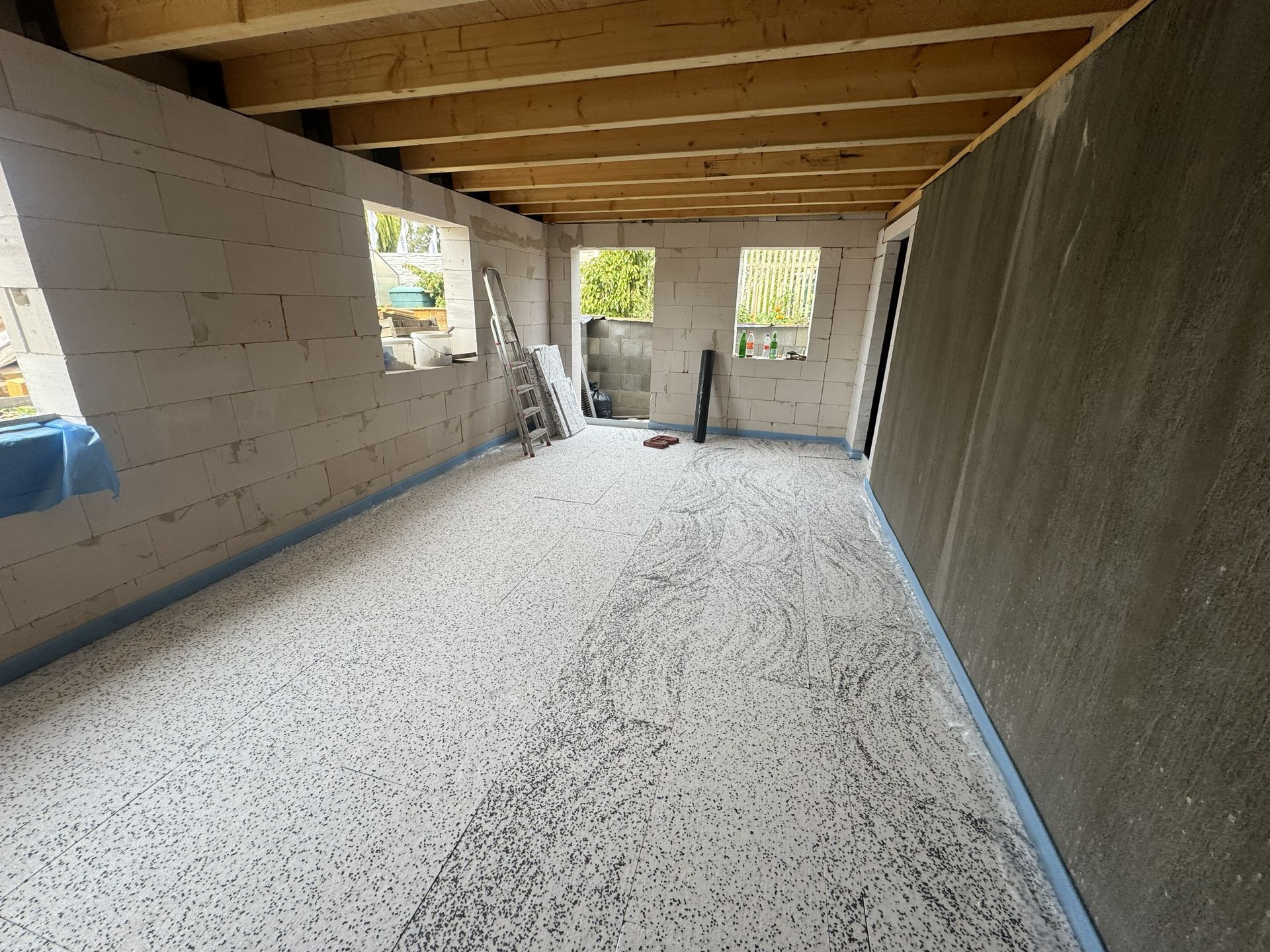 Teilweise fertiggestellter Raum mit Betonsteinwänden, freiliegenden Holzbalken an der Decke und einem Kiesboden