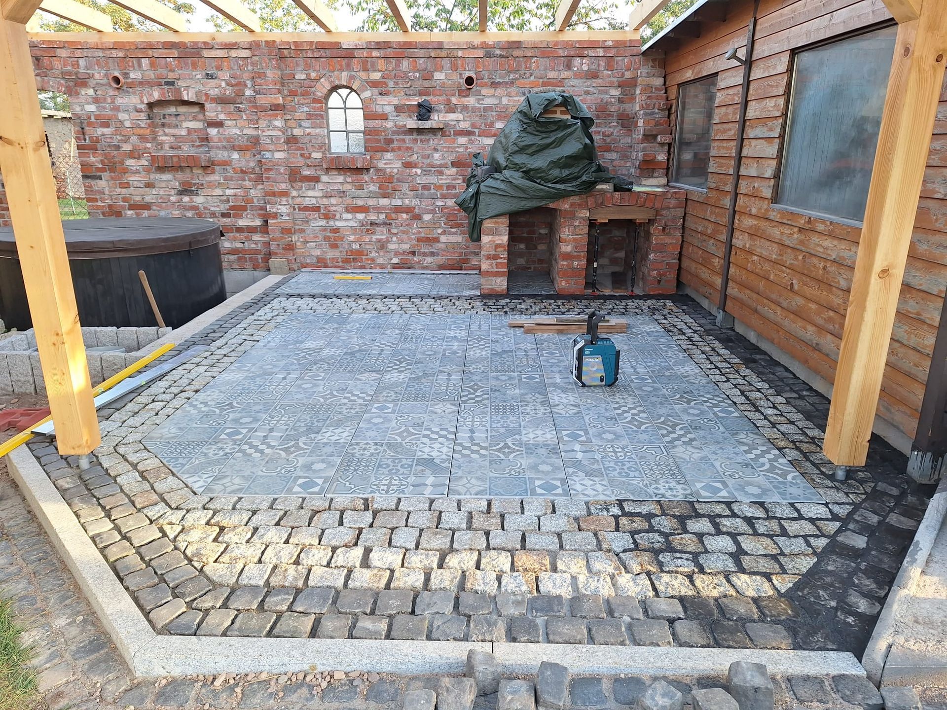 Mit Steinen gepflasterte Terrasse im Hinterhof mit Ziegelmauern, Holzpfosten und einem überdachten Grillplatz im Freien