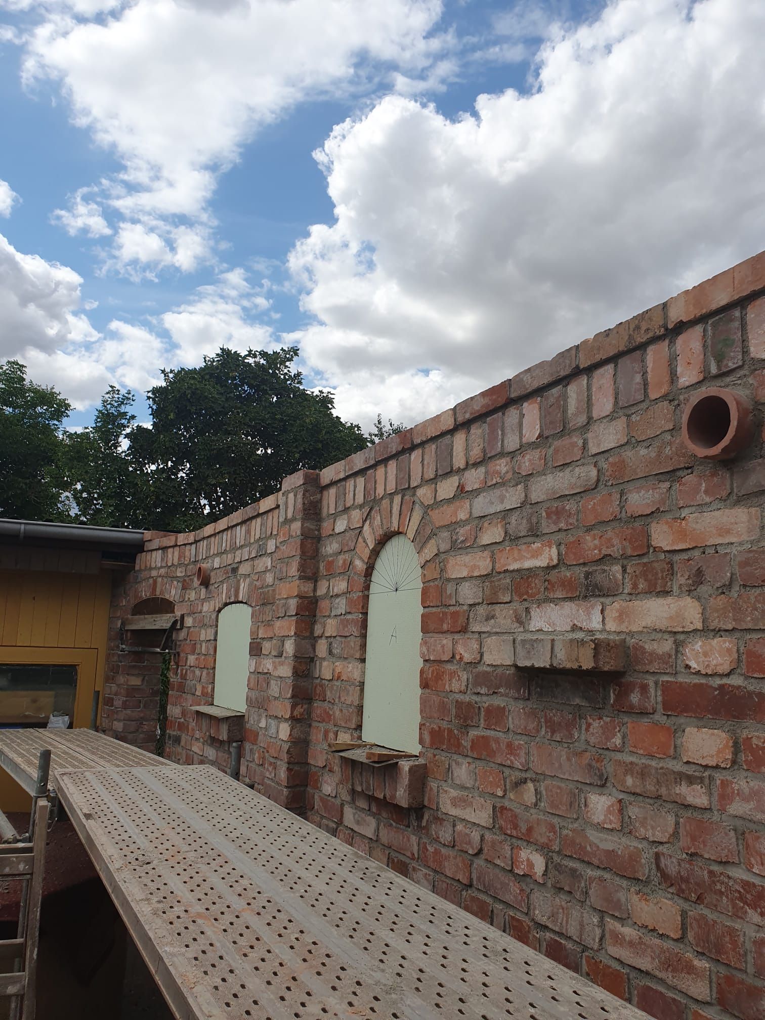 Backsteinmauer mit Bogennischen neben einem Metallsteg unter einem bewölkten Himmel