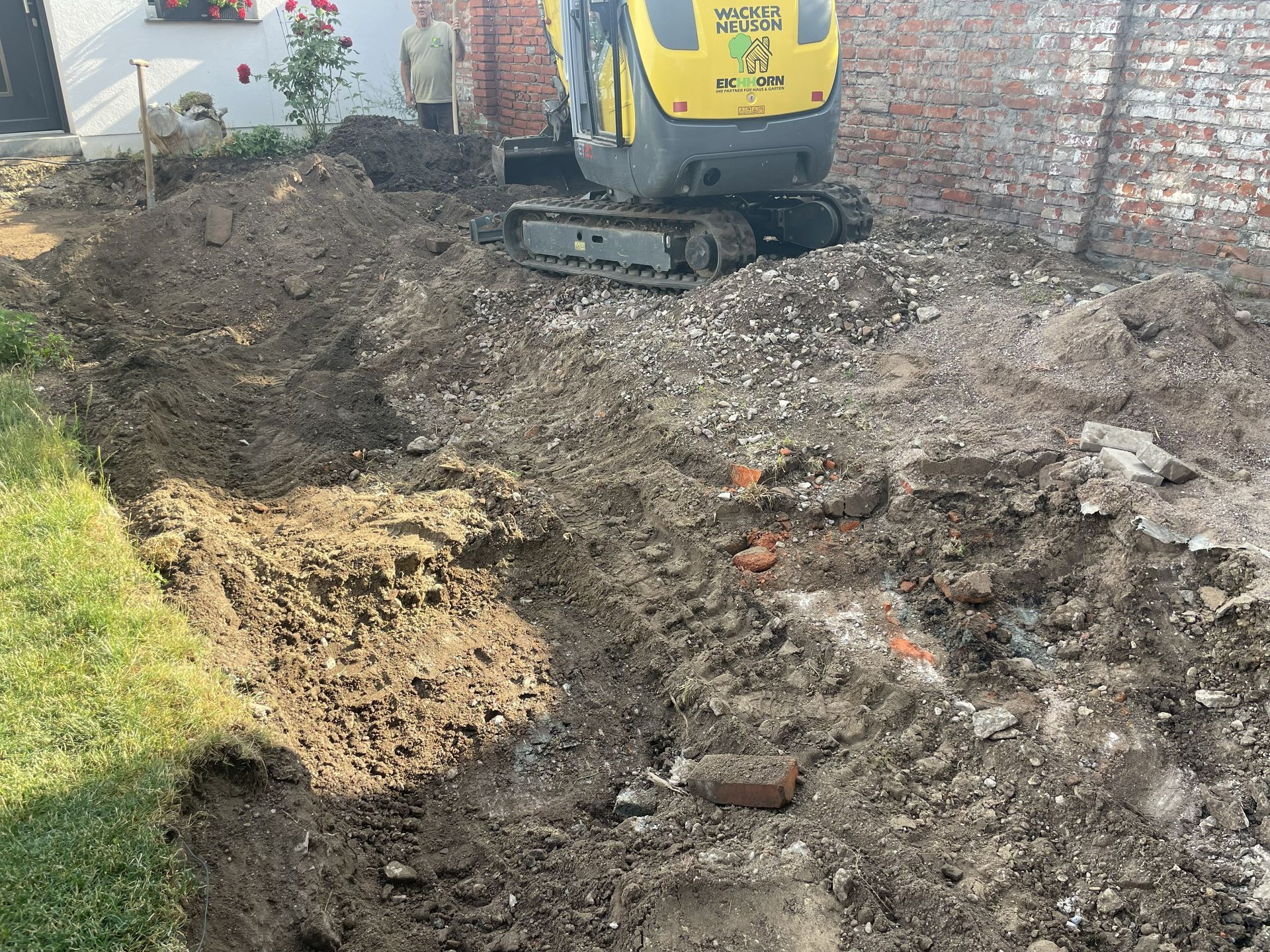 Ein Bagger gräbt einen schlammigen Graben neben einem Backsteinhaus und einem Rasen.