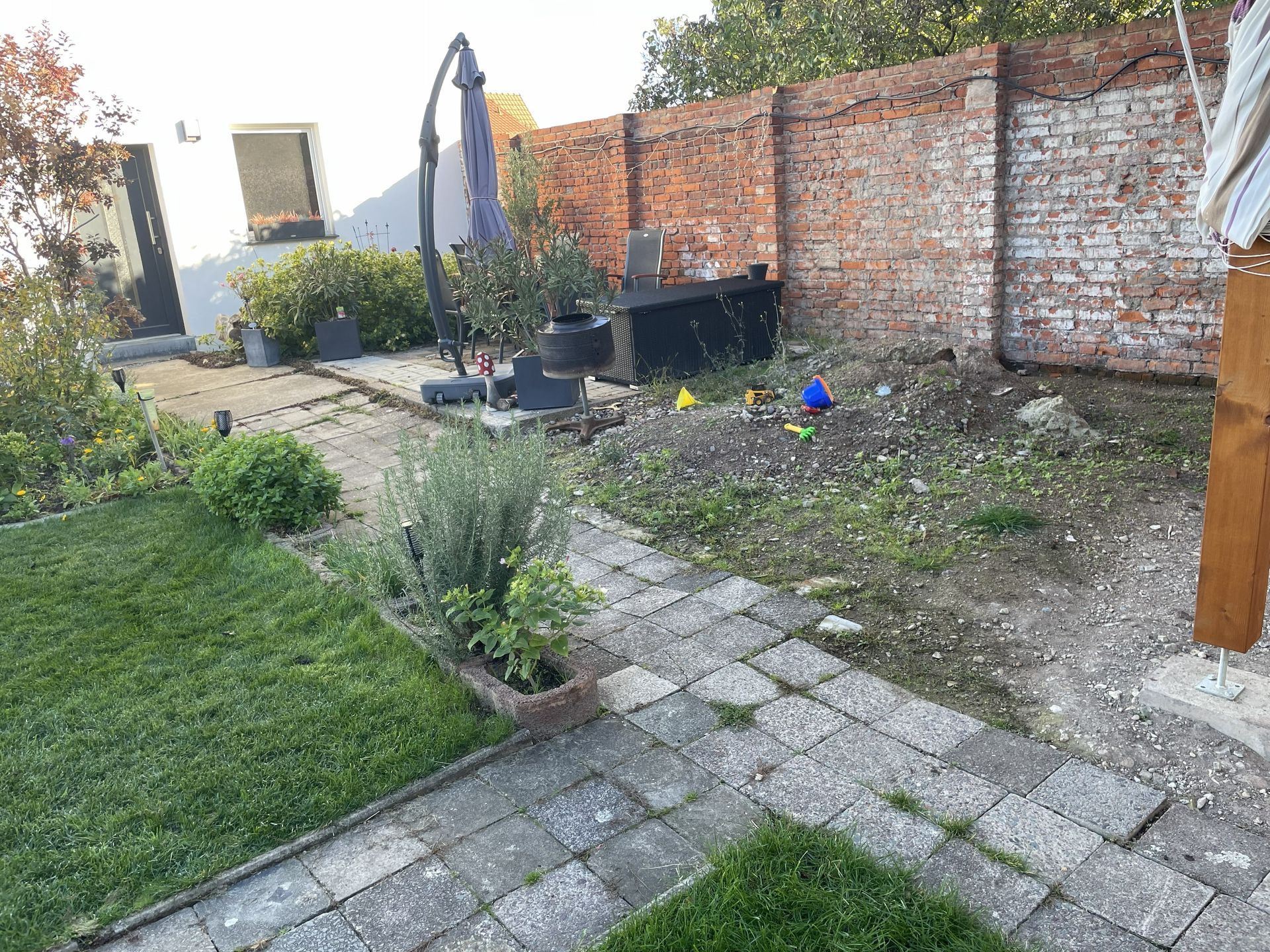 Hinterhofterrasse mit Backsteinmauer, Steinweg, Topfpflanzen, Sonnenschirm und Rasenfläche