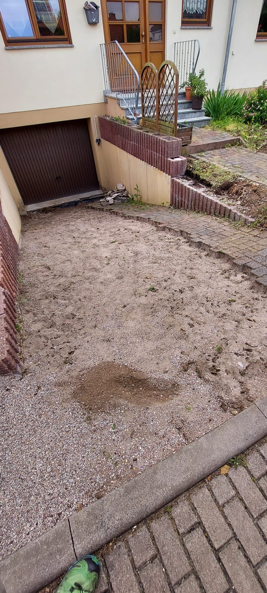 Kiesauffahrt neben einem Haus, im Vordergrund Garagentor und Ziegelpflaster.