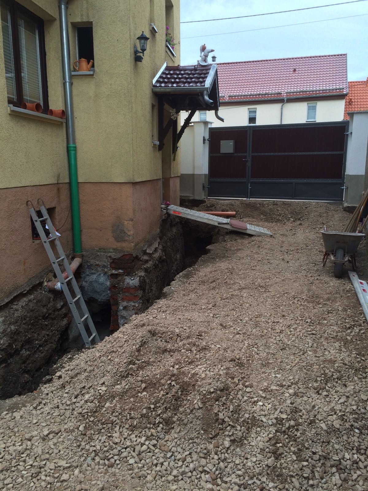 Schmaler Kiesweg neben einem Haus mit einem offenen Graben und einer an der Wand lehnenden Leiter.