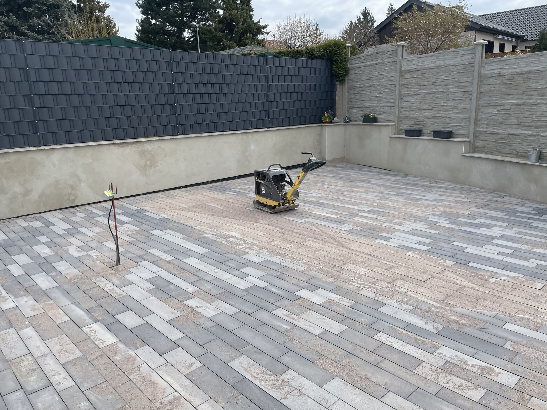 Hinterhofterrasse mit grauen Pflastersteinen und einer Verdichtungsmaschine in der Mitte während der Bauarbeiten