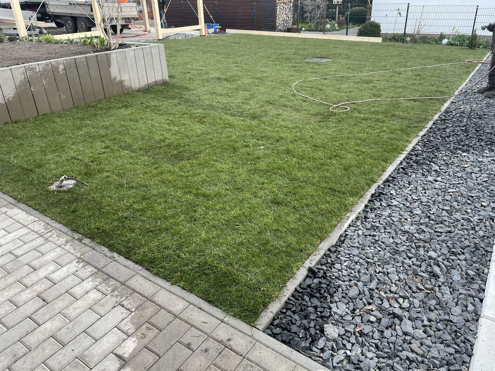 Kleiner Rasengarten, der von Pflastersteinen und einem dunklen Kiesstreifen im Freien begrenzt wird